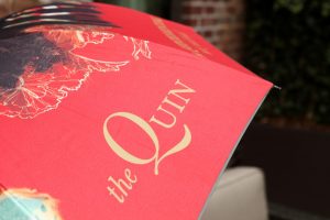 Quin brand name logo on umbrella, red and gold color palette, custom branded boutique hotel guest amenity
